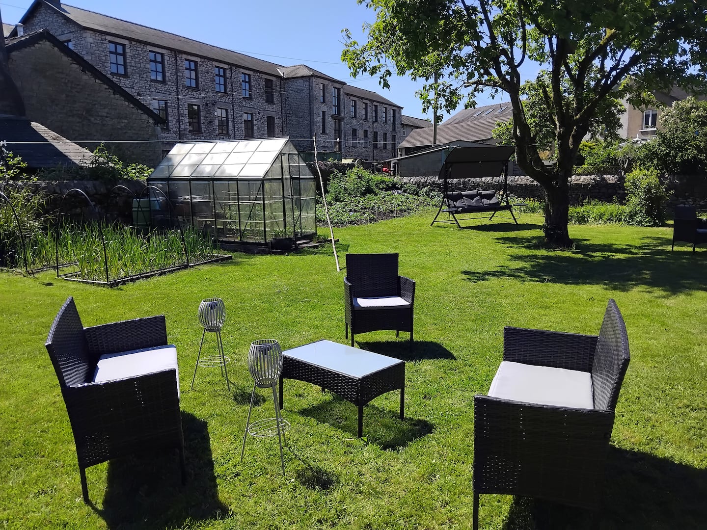 Outdoor chairs on the lawn with the greenhouse and garden swing beyond